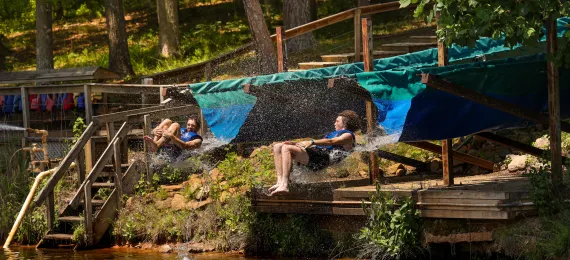 Two campers sliding off the slide at the same time, heading into the water